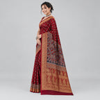 A woman modeling a richly patterned red and gold saree against a textured dark red backdrop with decorative gold leaf motifs.