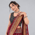 A woman wearing a red and gold patterned saree with a black printed blouse, posing against a textured dark red background with gold floral motifs.